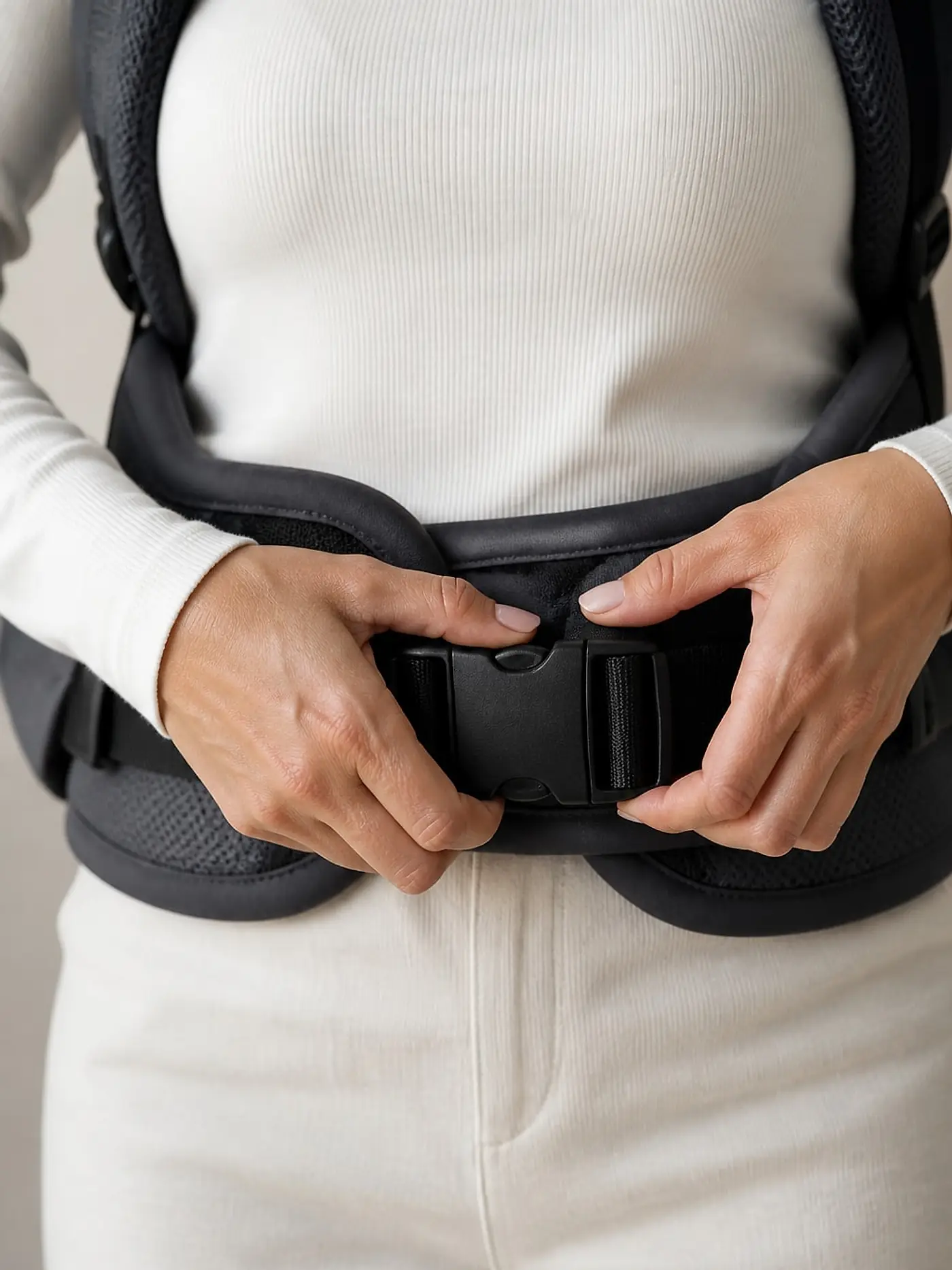 Manos ajustando la hebilla del cinturón lumbar de un portabebés sobre las caderas